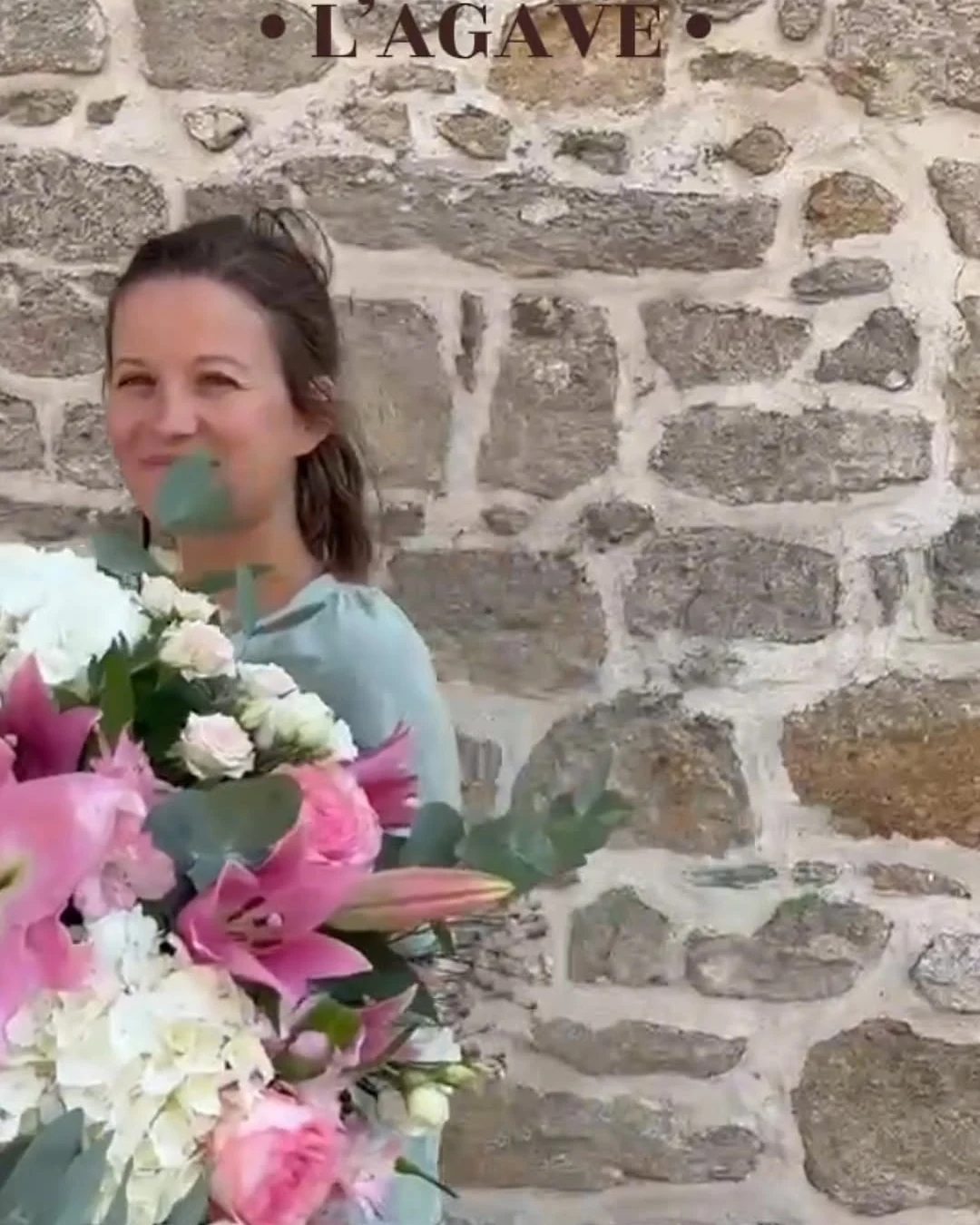 Laura devant la boutique, une brassée de lys et de roses roses dans les bras