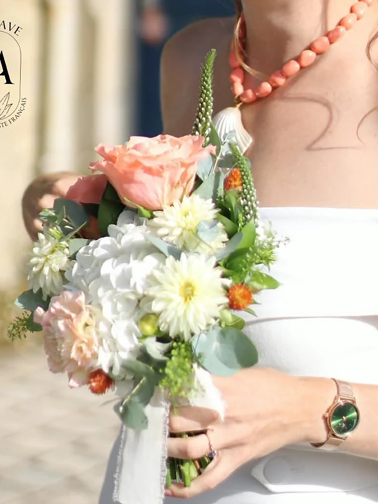 Une mariée tient son bouquet de roses pêche, hortensia et marguerites
