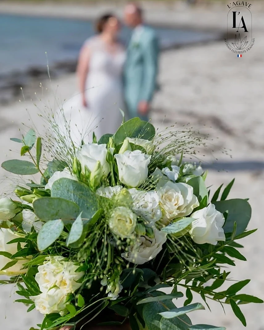 Les mariés sur la plage, un bouquet blanc et vert au premier plan